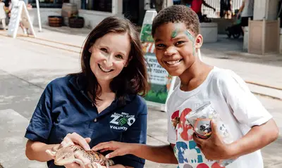 Volunteer and child smiling at the camera while the volunteer holds an exotic lizard